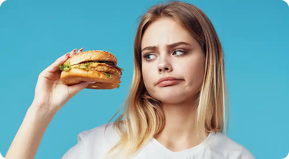 Girl looking at a burger, wondering is she should eat it or start eating healthier 